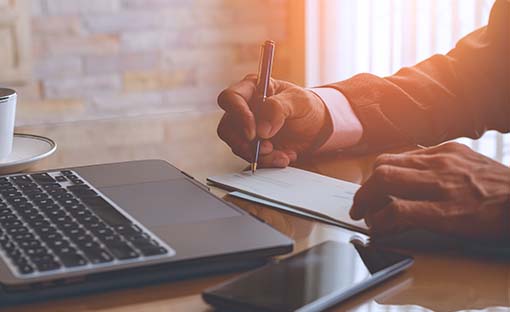 Man filling out a check, sitting in front of an open laptop