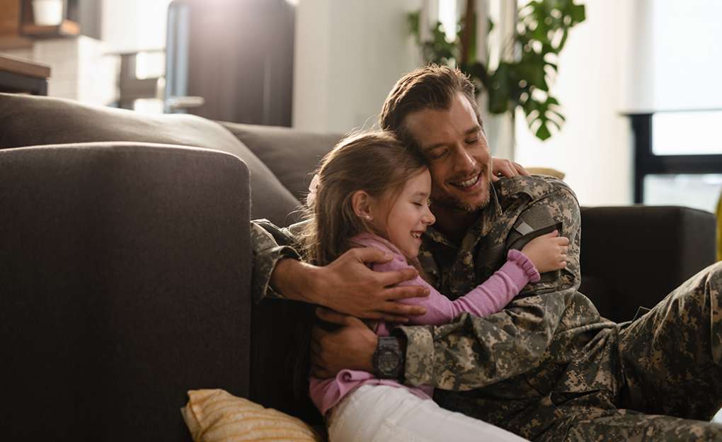 A uniformed soldier hugs his young daughter.