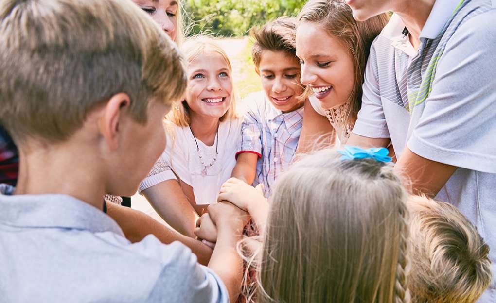 A group of young children with their hands in a circle, symbolizing teamwork