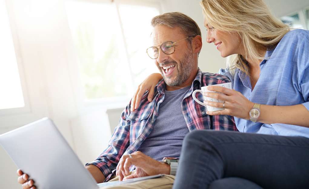 A middle aged couple look at a laptop on the couch and smile.