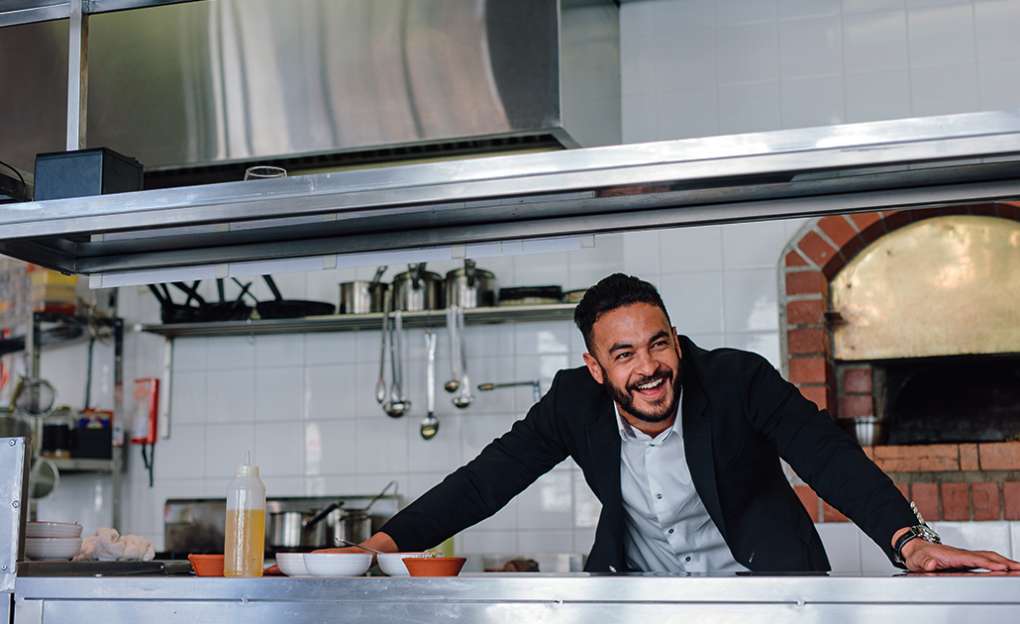 A man in a suit laughs behind the counter of a professional kitchen.