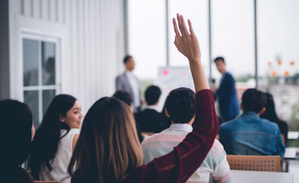 A young student raising her hand in a lecture setting