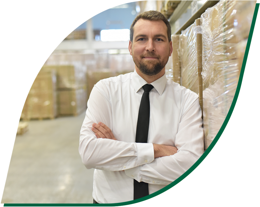 An image of a man wearing a shirt and tie leaning against a stack of boxes inside a warehouse.
