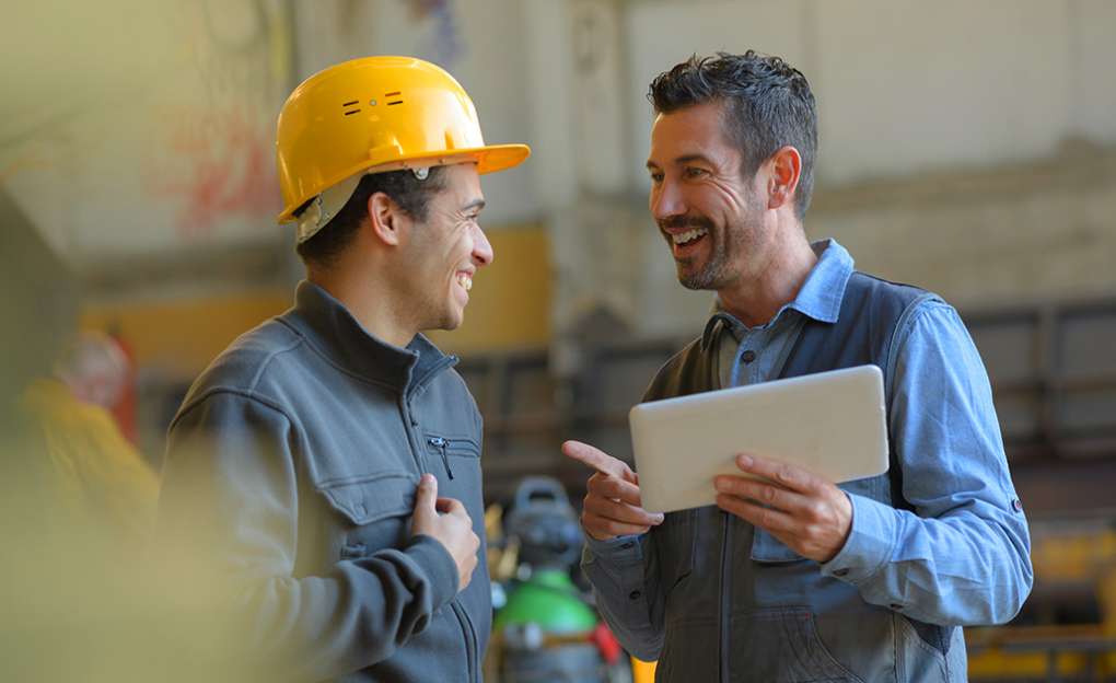 A man in a hard hat converses with a man in business clothing.