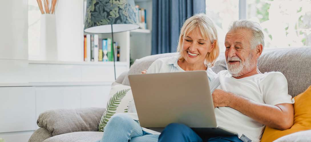 An older couple review checking accounts on their laptop.