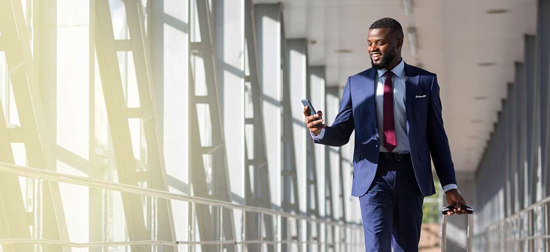 A young businessman wearing a suit and tie looks at his phone while smiling.