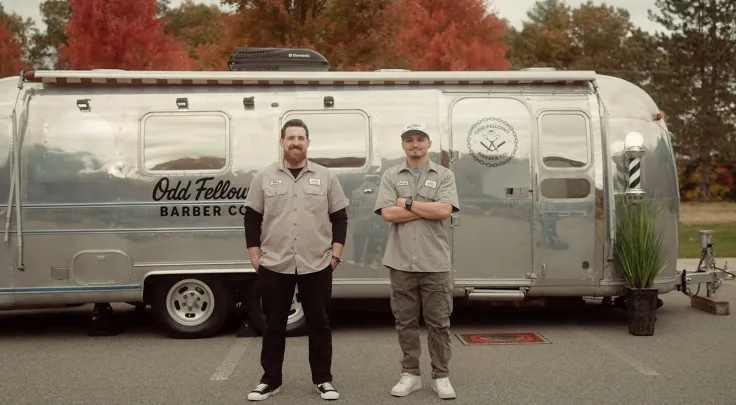Two North Easton Savings Bank local business partners standing in front of an airstream trailer that has Odd Fellows Barber Co. written on the side of it